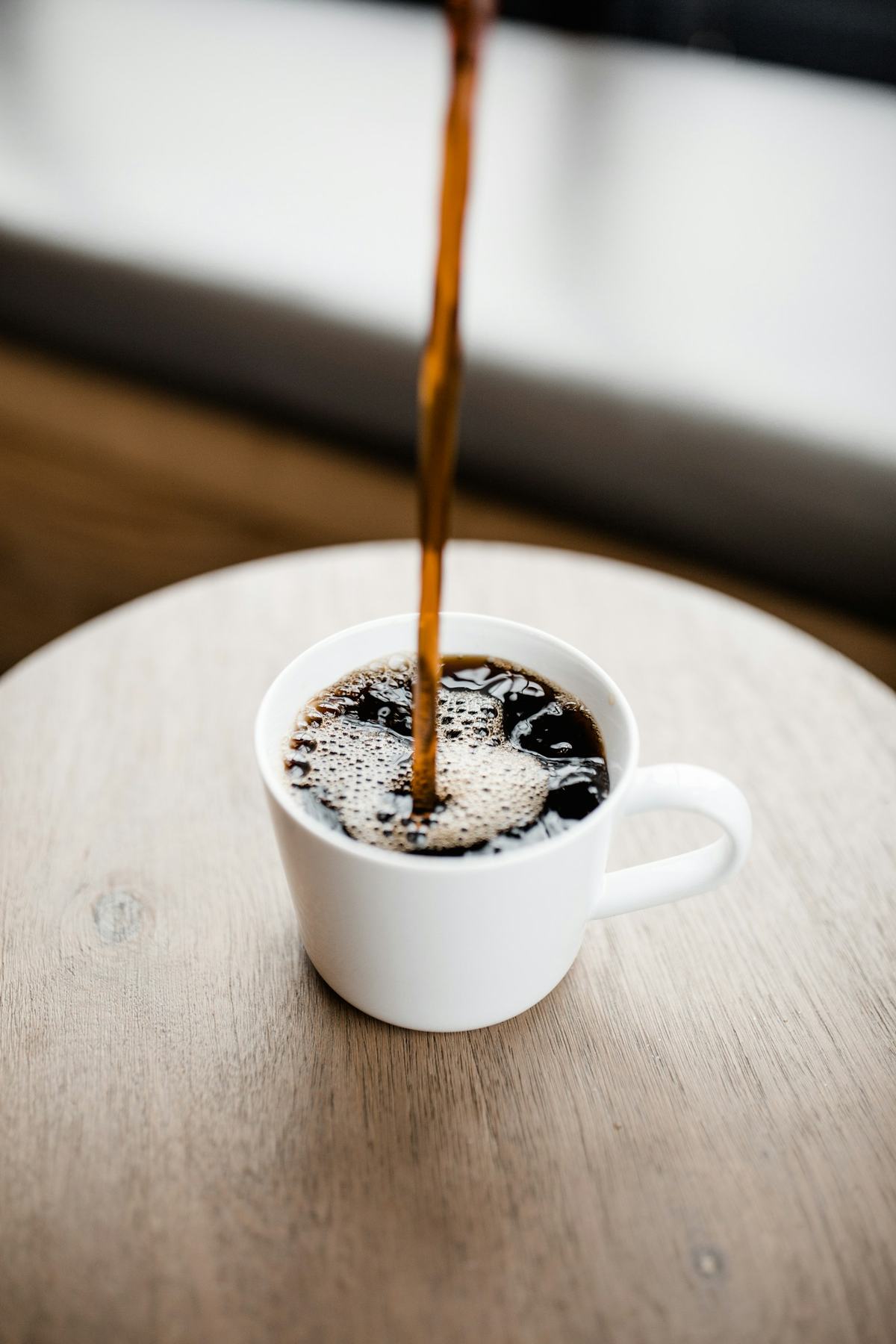 Kaffee wird in eine weiße Tasse auf einem hellen Holztisch gegossen